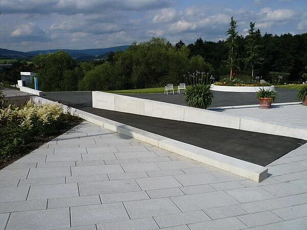 Geneigte Erschließungsfläche auf der Bayerischen Gartenschau „Natur in Waldkirchen“ 2007. Die geneigte Ebene ist gegenüber der Umgebung visuell kontrastreich markiert. Mitlaufende Betonwangen dienen als Radabweiser.